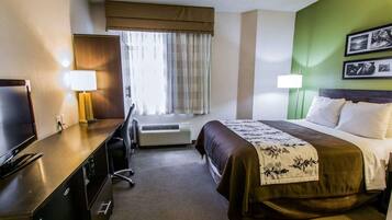 Quarto de hotel com cama, secretária com televisão, luminária, janela com cortinas, ar condicionado e parede verde de destaque.