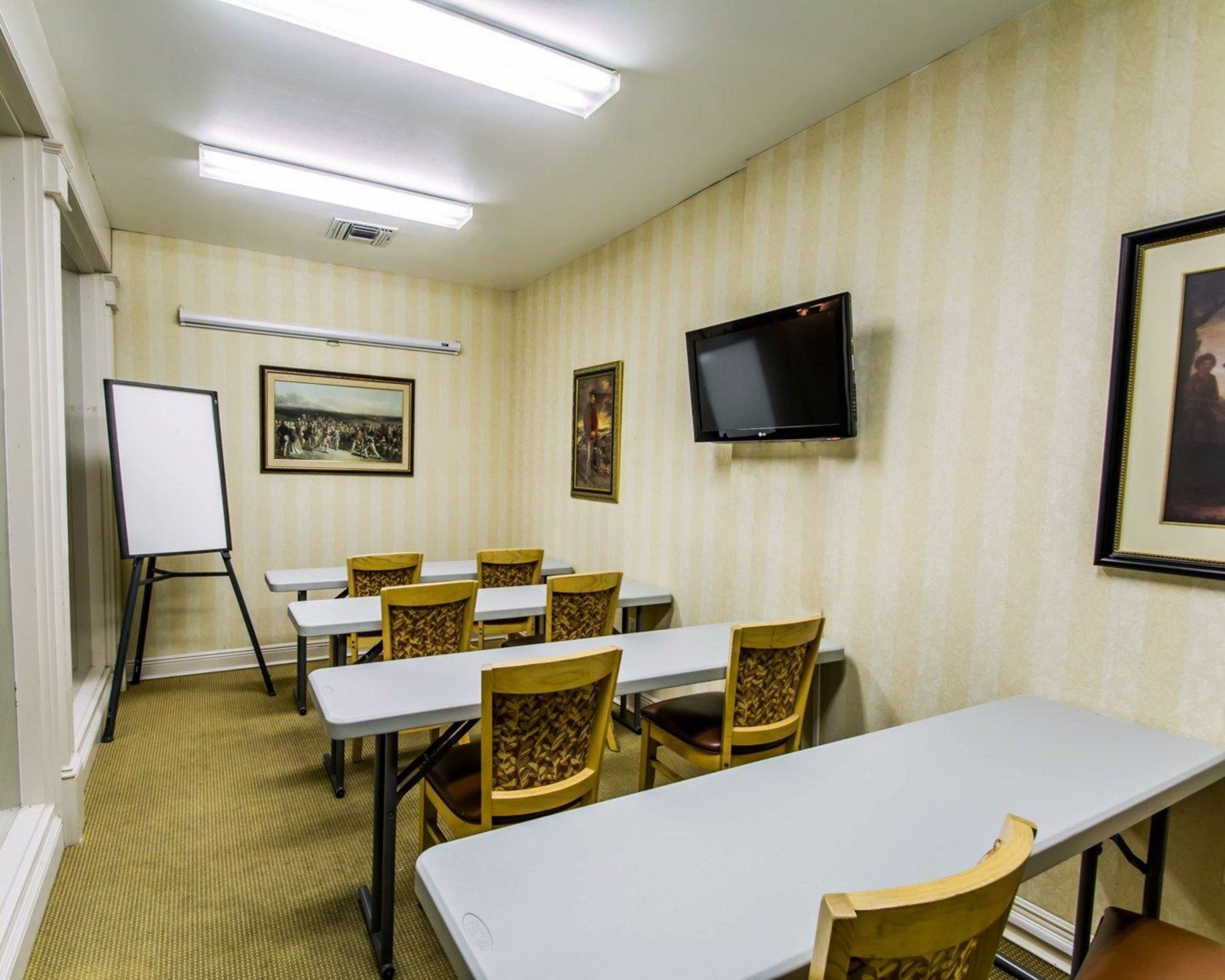 A conference room with tables and chairs, a whiteboard, a television, and framed pictures on the walls.