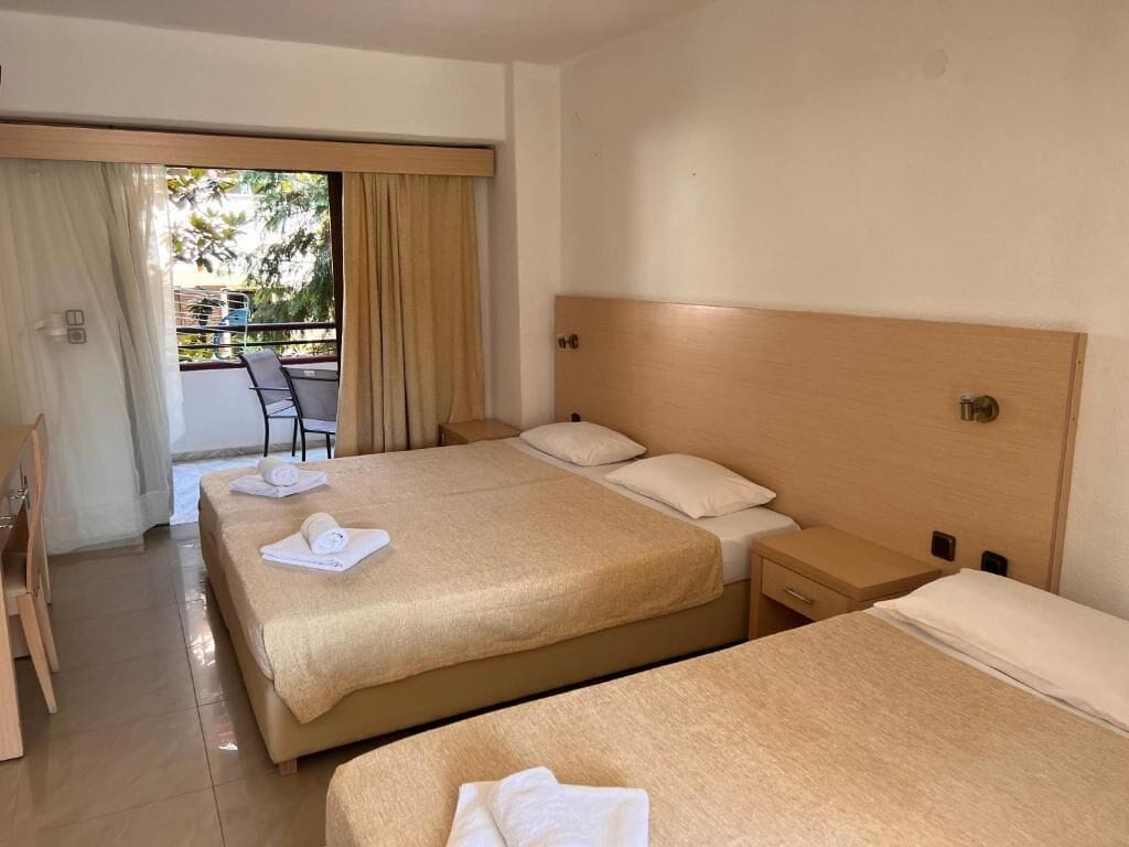 A hotel room with two beds, a balcony, and a view of the outdoors.