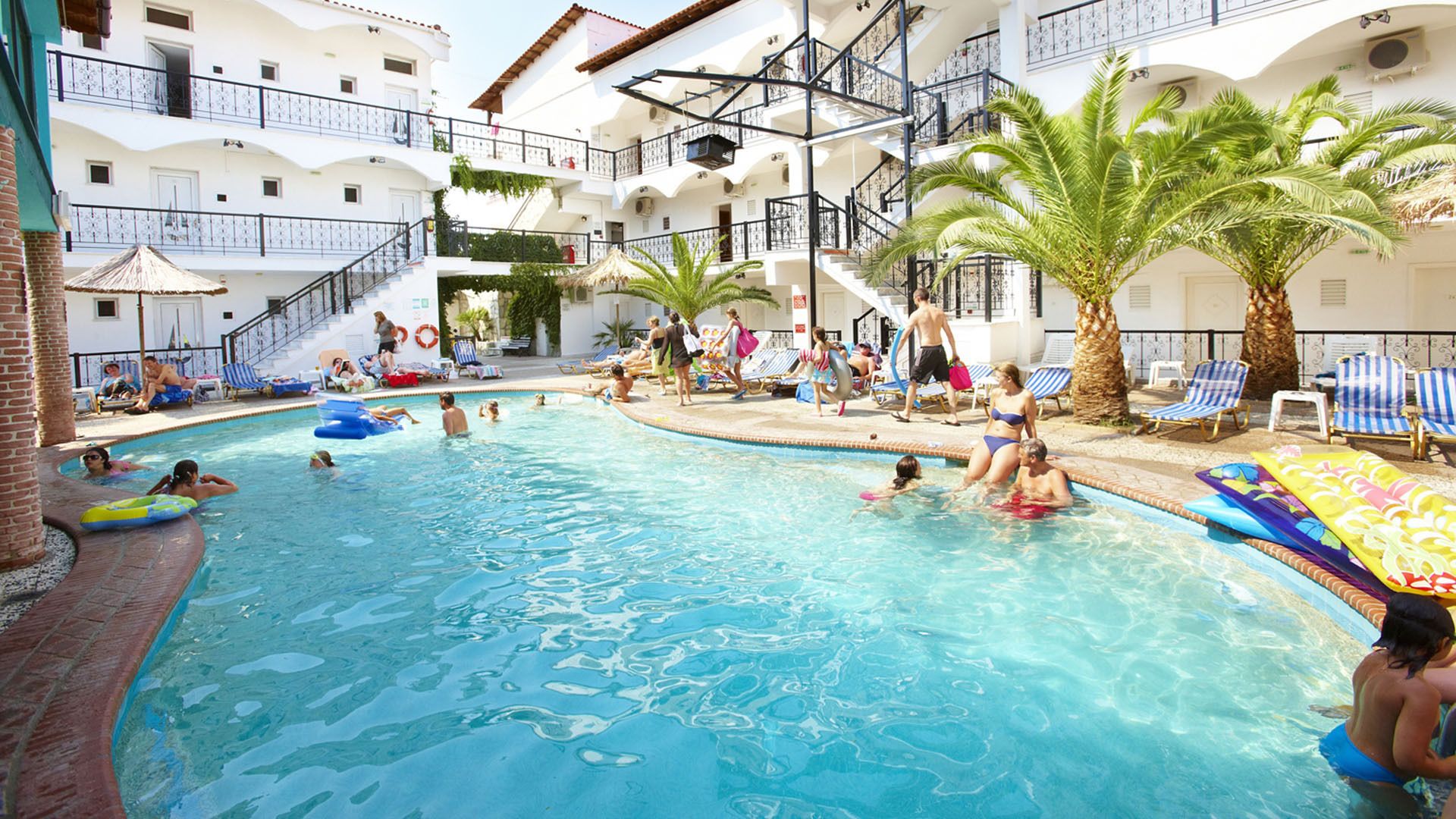 A swimming pool area with multiple levels of balconies, palm trees, and lounge chairs.