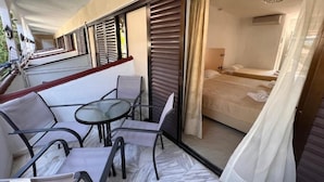 A balcony with a glass table and chairs, a sliding door to a bedroom, and a view of the outdoors. - Hanioti Grand Victoria (Kassandra)