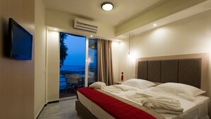 Una habitación de hotel con cama, televisor, puerta corrediza al balcón y aire acondicionado.