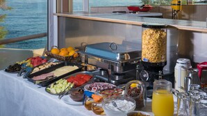 Una mesa de buffet con diferentes alimentos y un dispensador de jugo, con vista panorámica al océano.