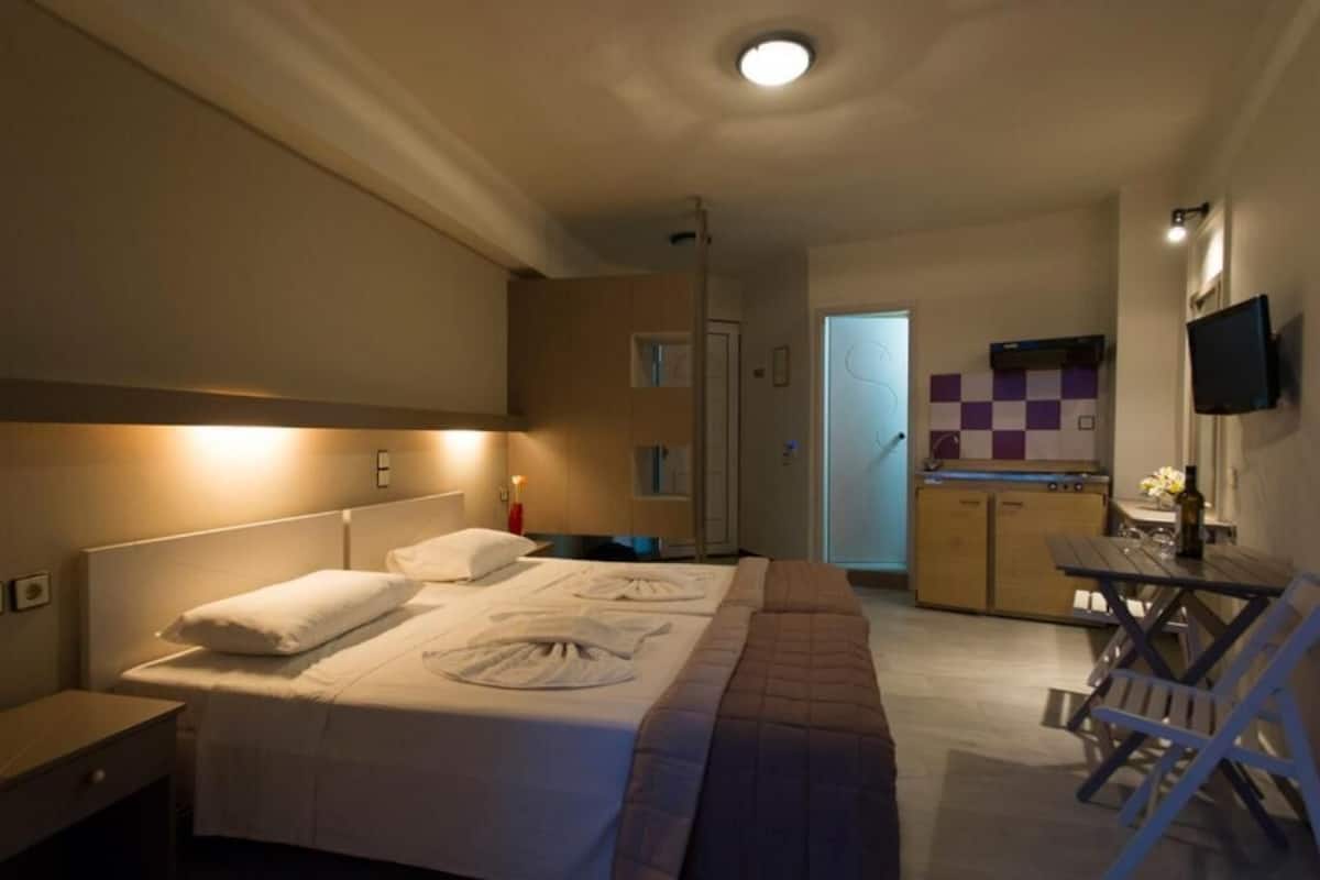 A hotel room with a bed, bedside table, and a kitchenette area with a TV and a small table.
