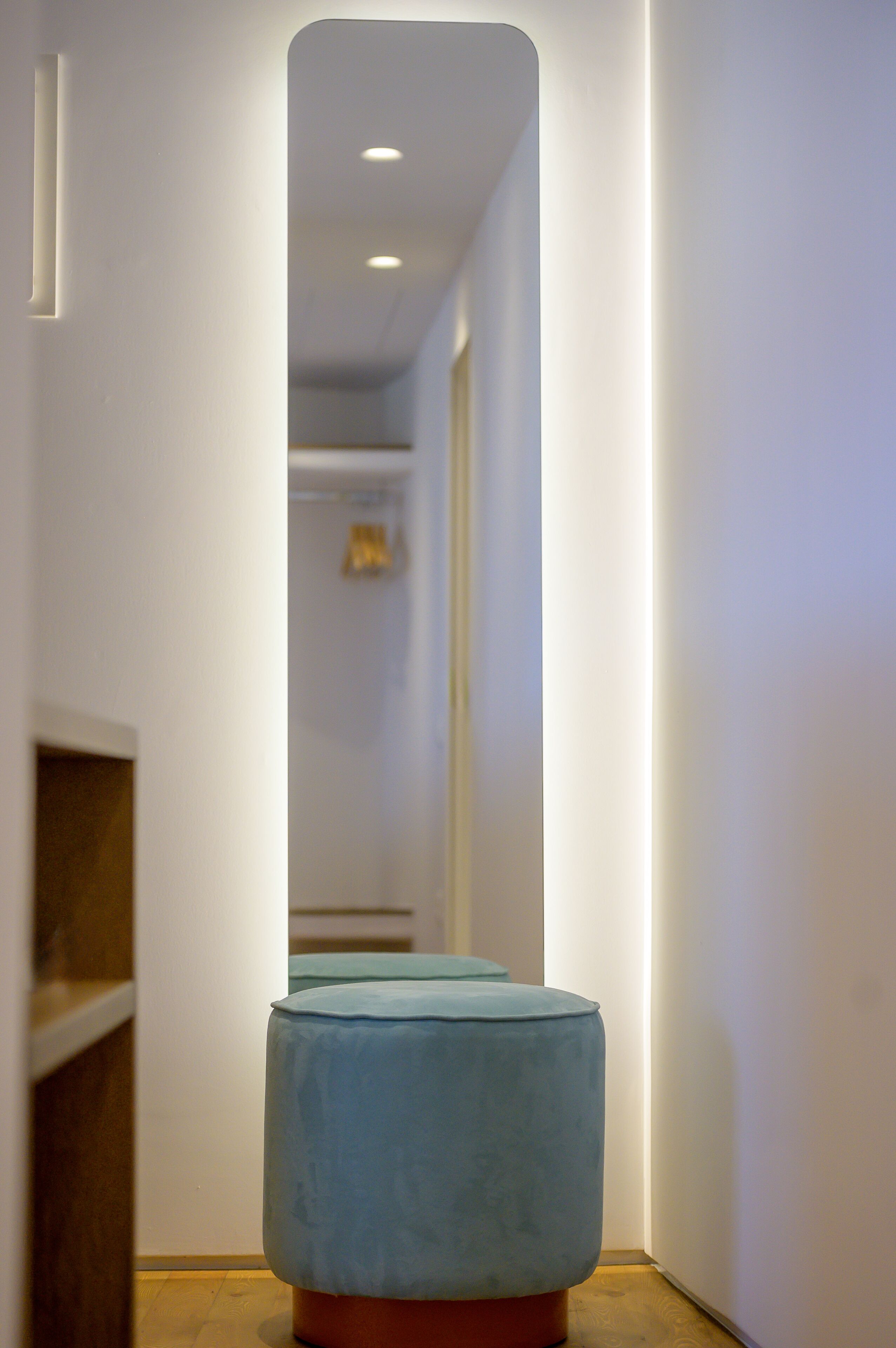 Un couloir étroit avec un pouf bleu clair et un banc en bois.