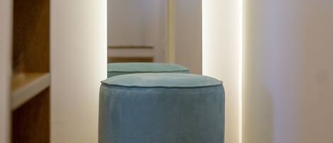 Un couloir étroit avec un pouf bleu clair et un banc en bois.