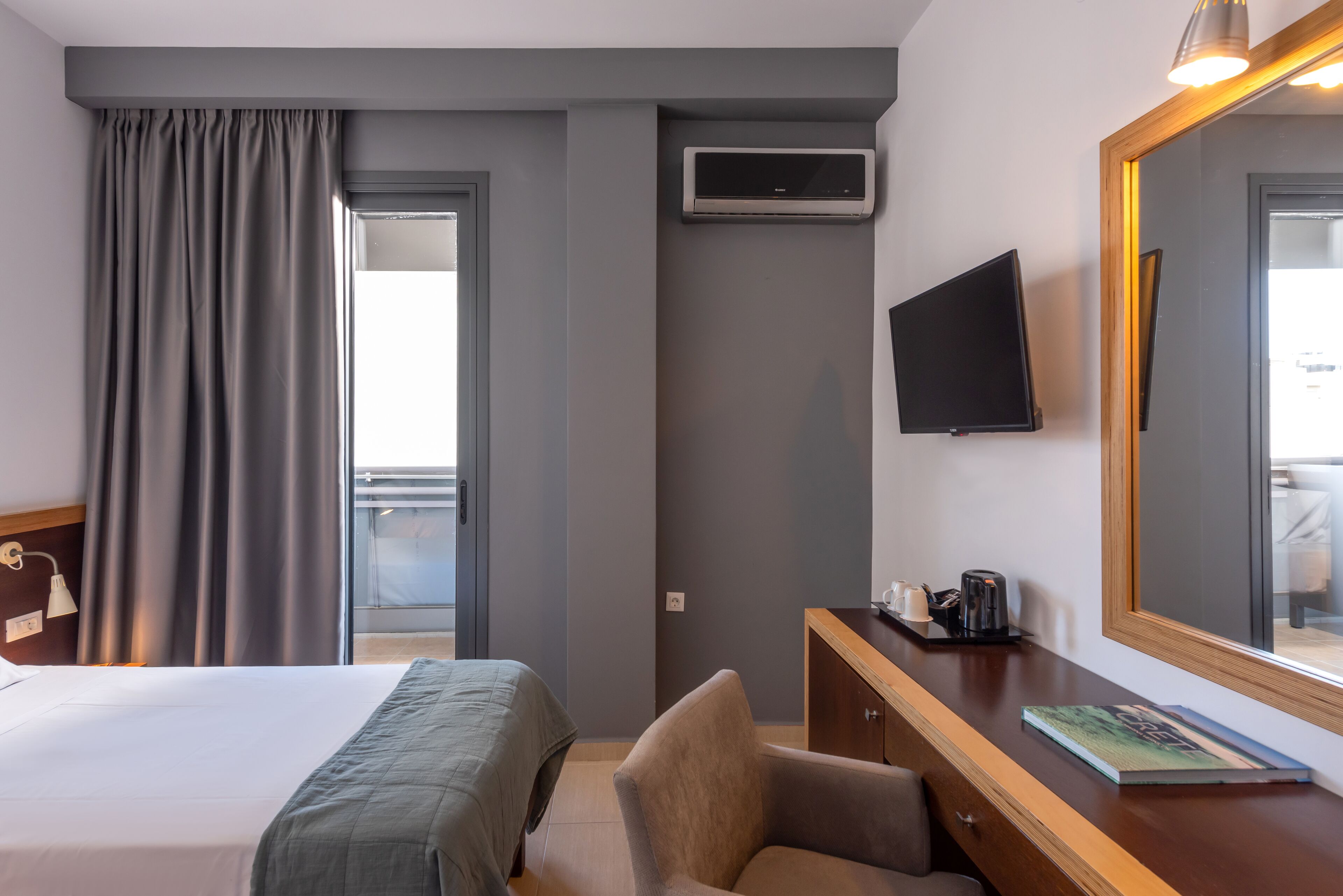 A hotel room with a bed, a desk with a chair, a TV, and an air conditioning unit.