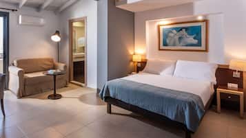 A hotel room with a bed, a sofa, a small table, a lamp, and a painting on the wall.