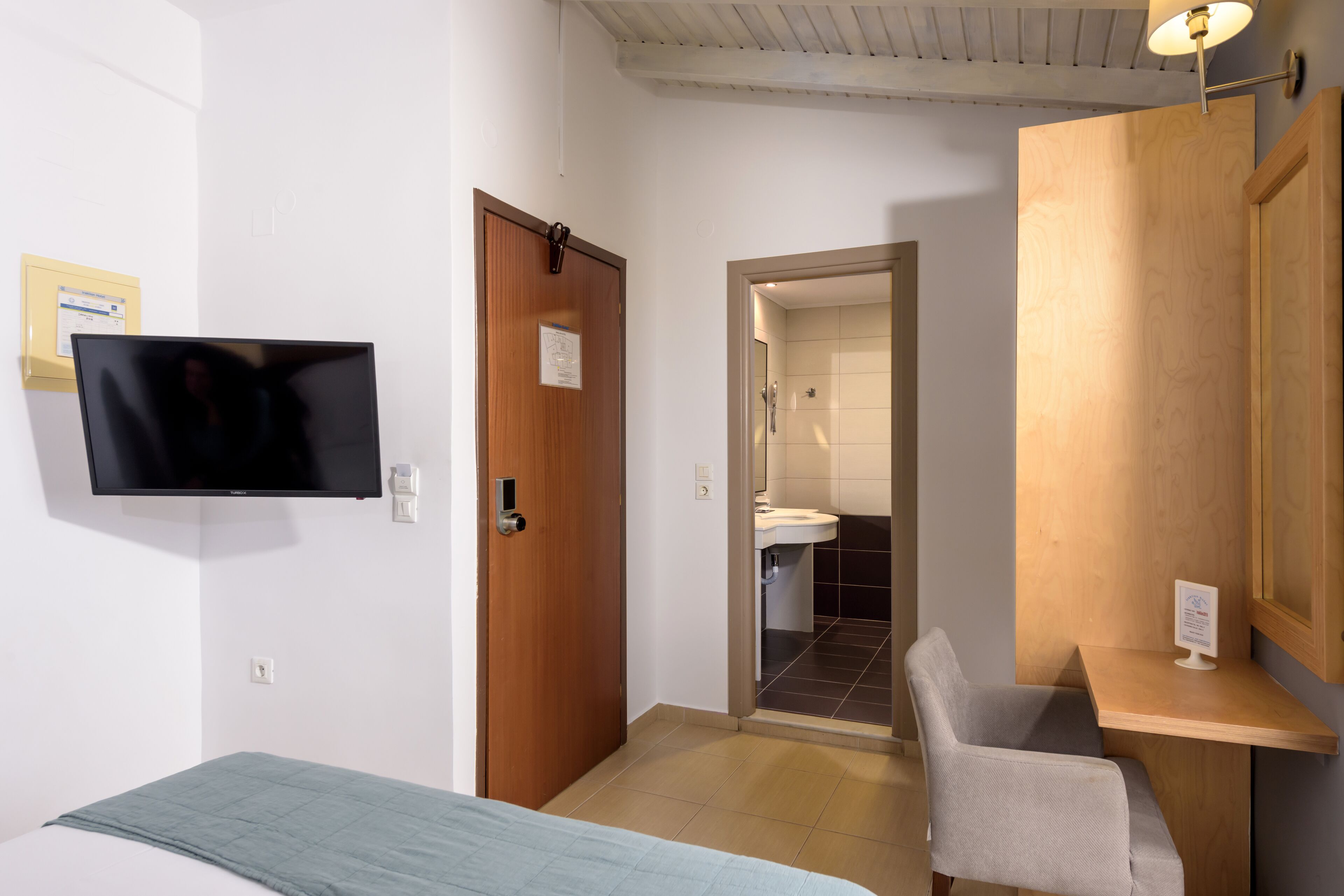A hotel room with a bed, a desk, a chair, a television, and a bathroom visible through an open door.