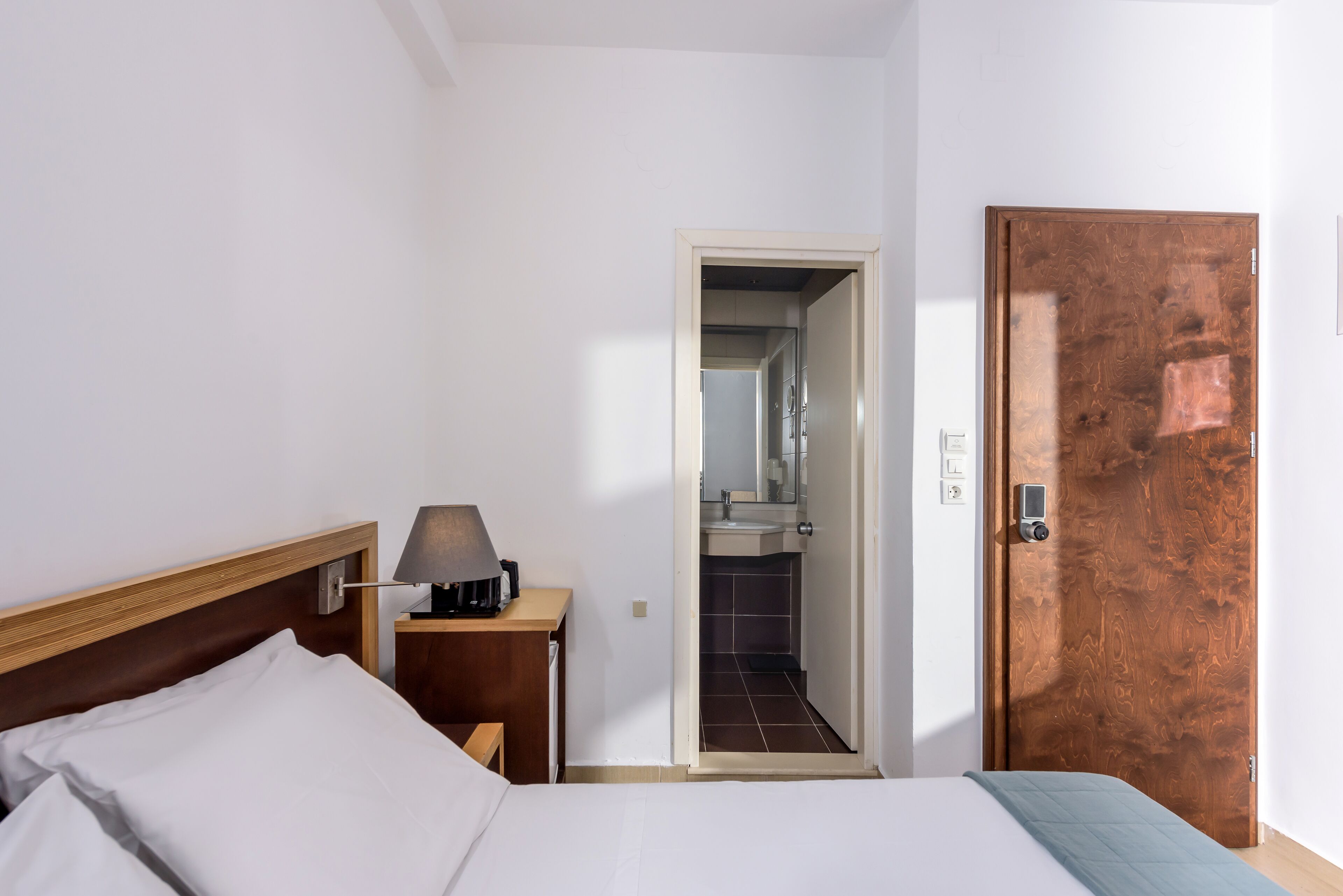 A hotel room with a bed, bedside table, lamp, and a door leading to a bathroom.