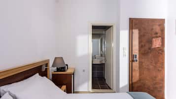 A hotel room with a bed, bedside table, lamp, and a door leading to a bathroom.