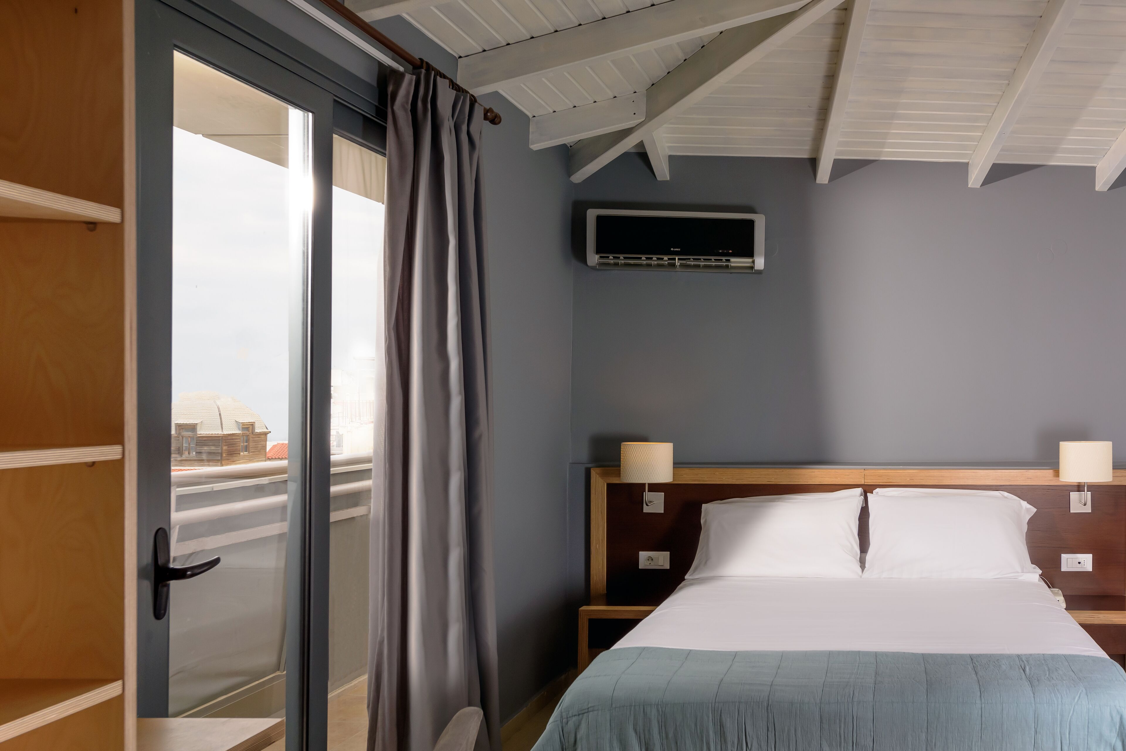 Une chambre d’hôtel avec un lit, un climatiseur fixé au mur et une vue à travers une porte vitrée.