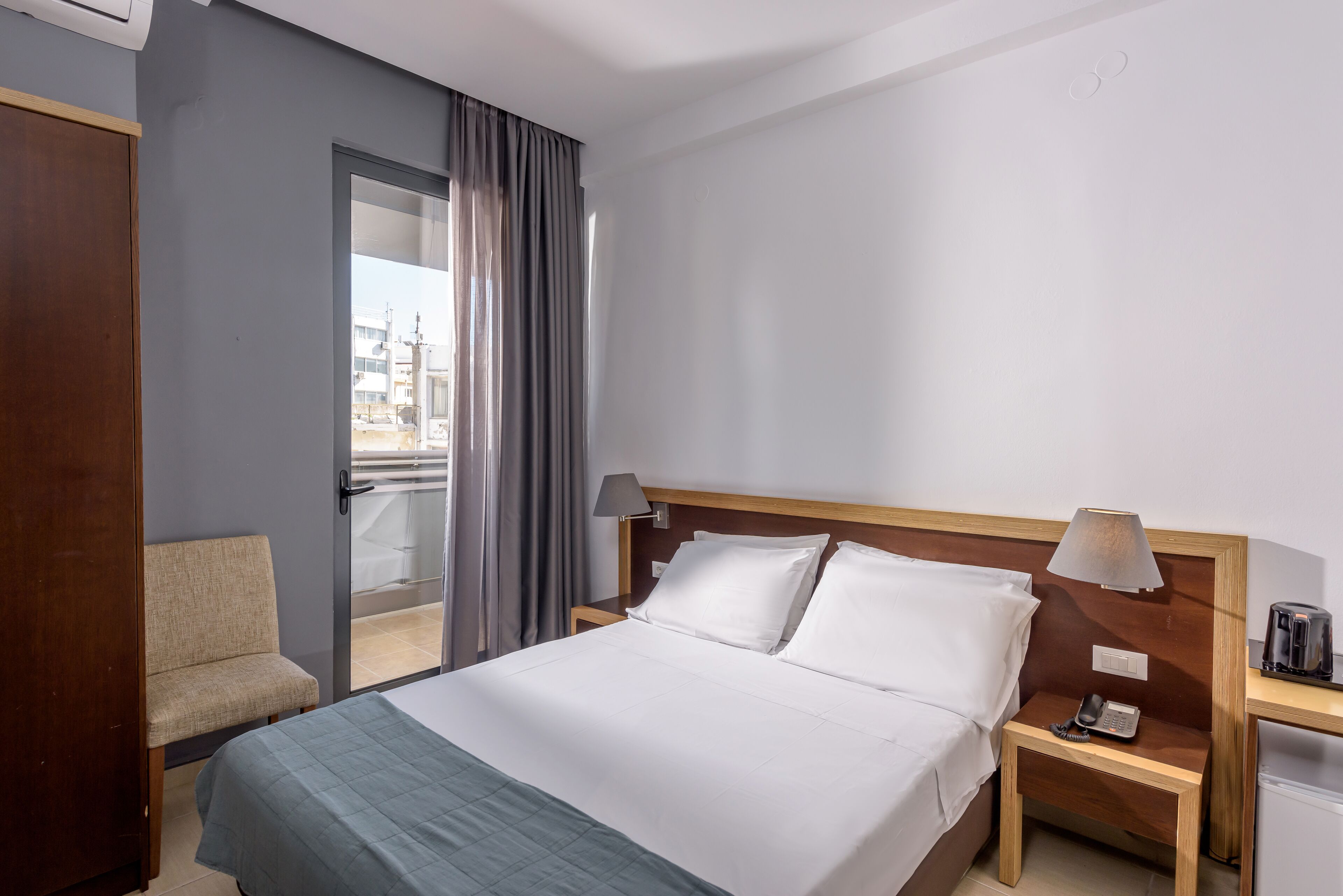 Une chambre d’hôtel avec un lit, une chaise, une table de chevet avec une lampe et une vue sur la ville par la fenêtre.