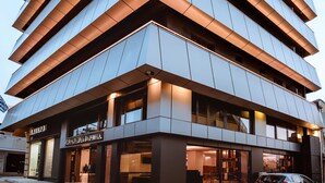 A modern multi-story building with a unique angular design, featuring large windows and a car parked in front. - Iraklion Hotel (Heraklion)