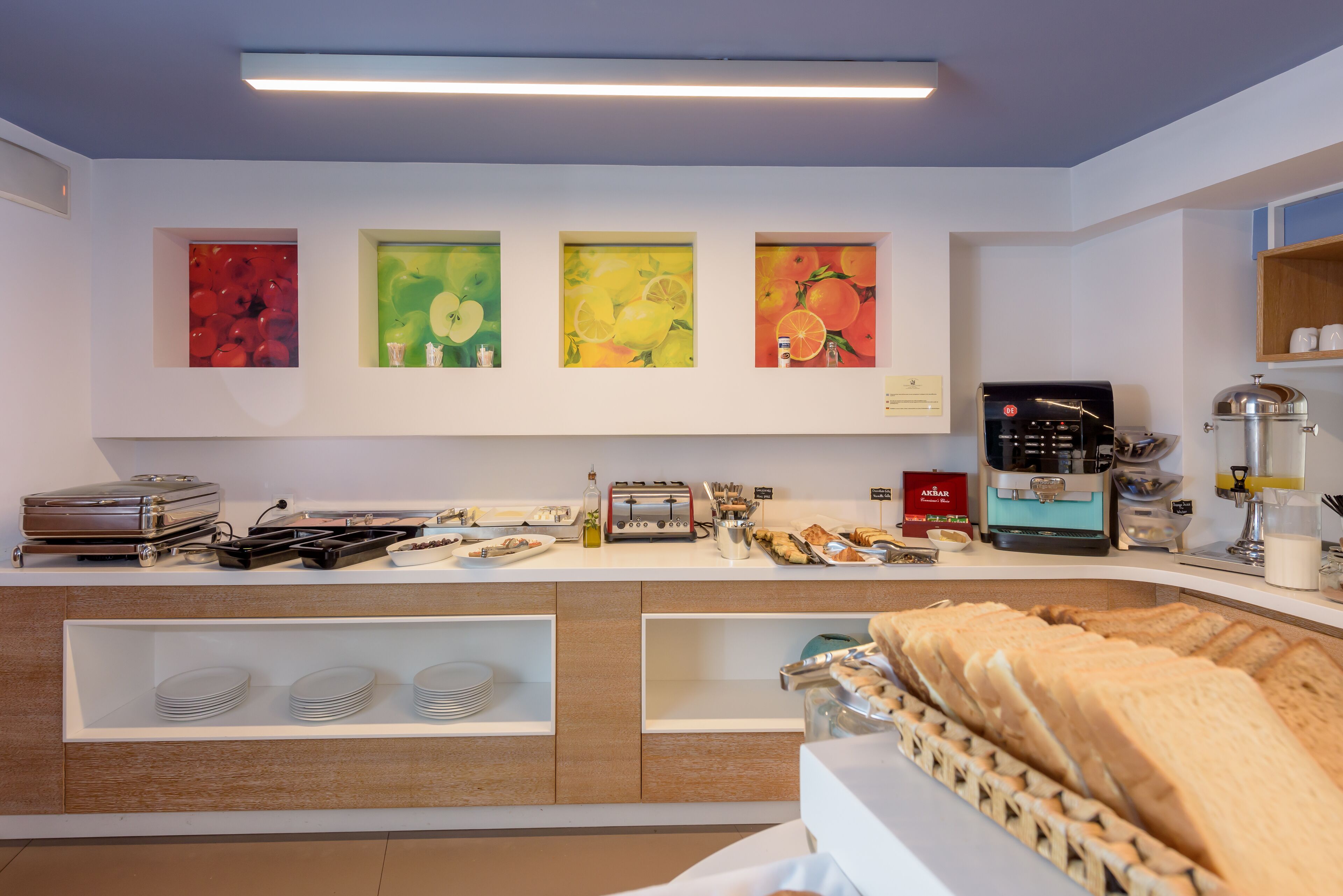 Ein Frühstücksbuffet mit verschiedenen Speisen, einer Kaffeemaschine und Kunstwerken an der Wand.