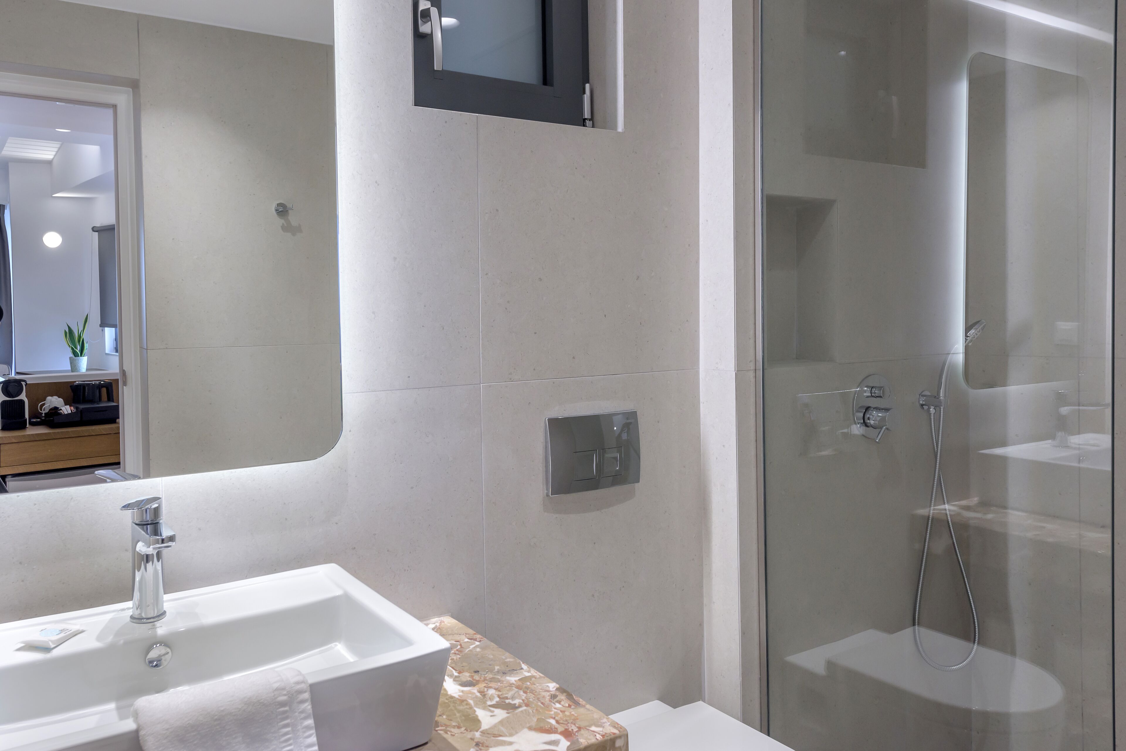 Een moderne badkamer met een wit wastafelmeubel, een marmeren blad, een douchecabine met glazen wanden en een spiegel boven het wastafelmeubel.