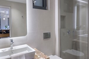 Un bagno moderno con un lavandino bianco, un piano di lavoro in marmo, una cabina doccia in vetro e uno specchio sopra il lavandino.
