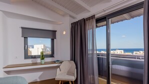 A modern room with a large window, a chair, a small table with a plant, and a bed. - Iraklion Hotel (Heraklion)