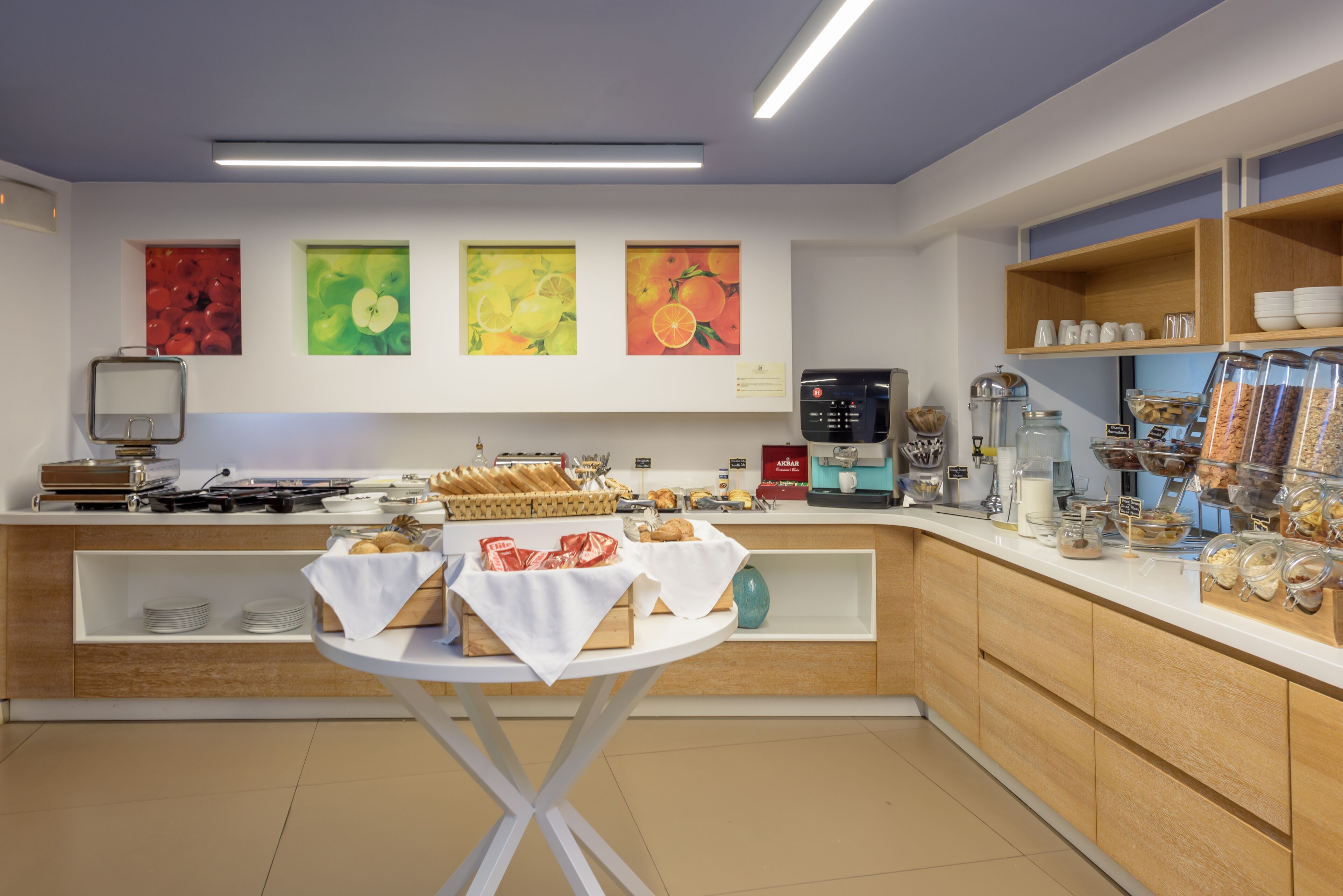 A modern breakfast area with a buffet setup, including bread, pastries, and beverages.