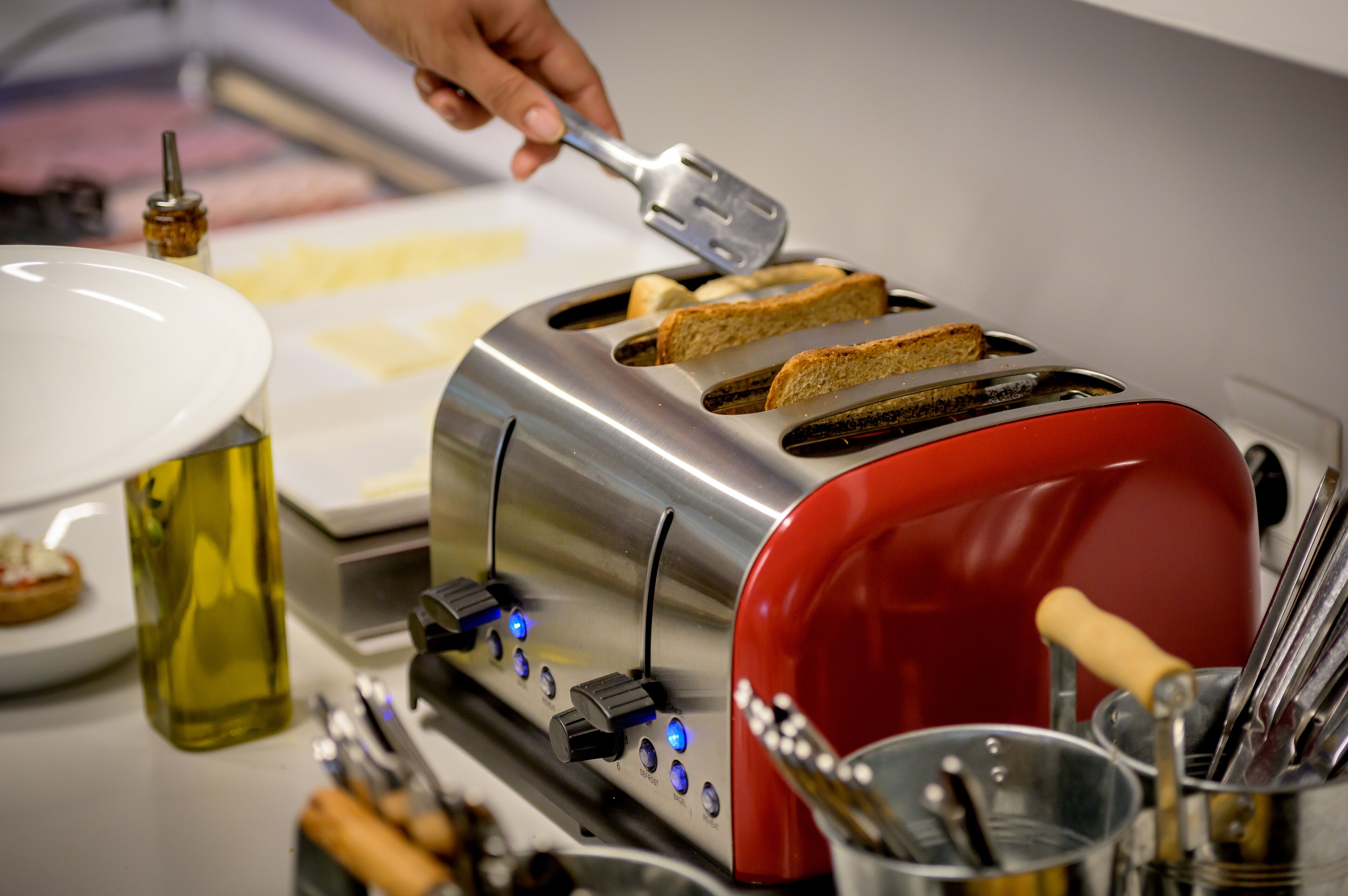 A kitchen with a red toaster, a white plate with toast, and a bottle of olive oil.