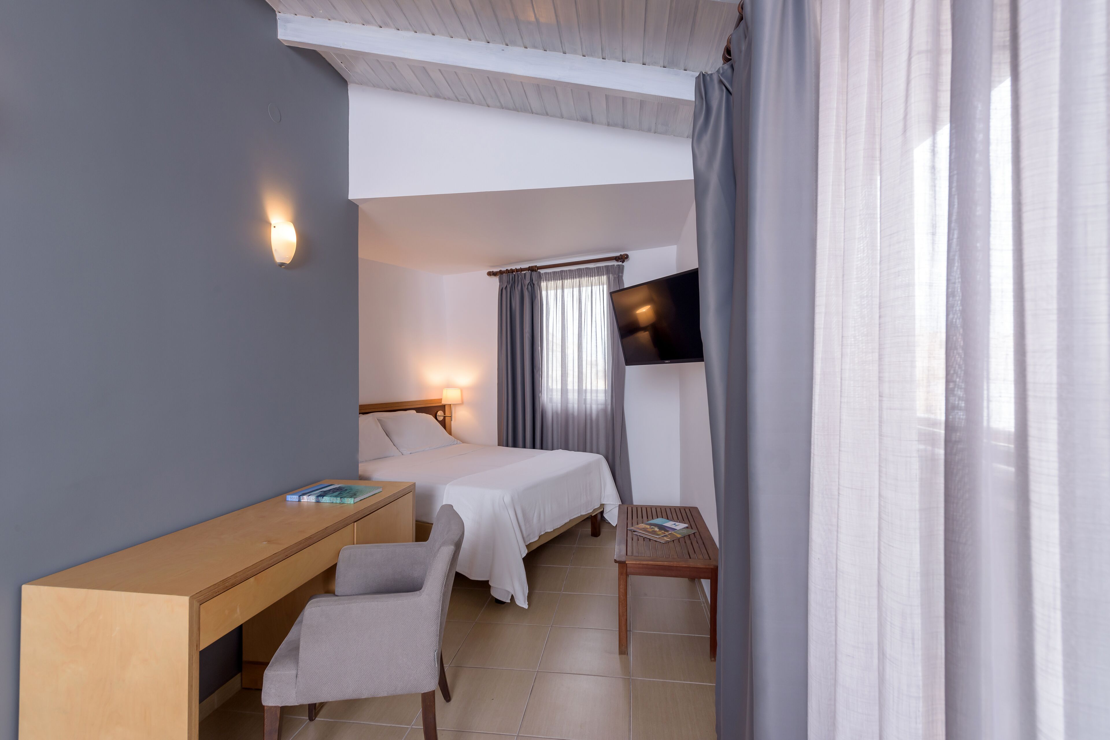 A hotel room with a bed, a desk, a chair, a TV, and curtains.