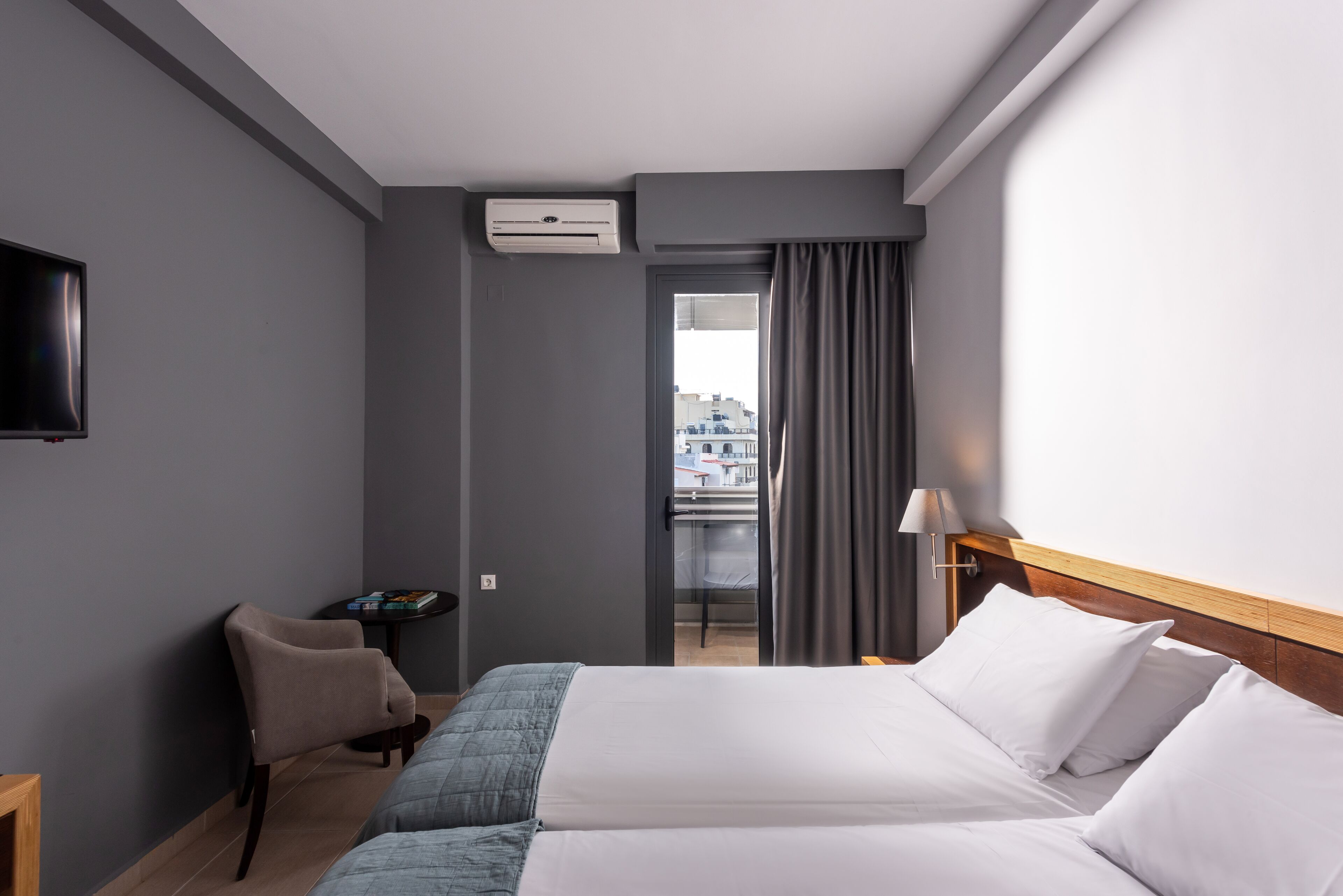 A hotel room with a bed, a chair, a small table, a TV, and a window with curtains.