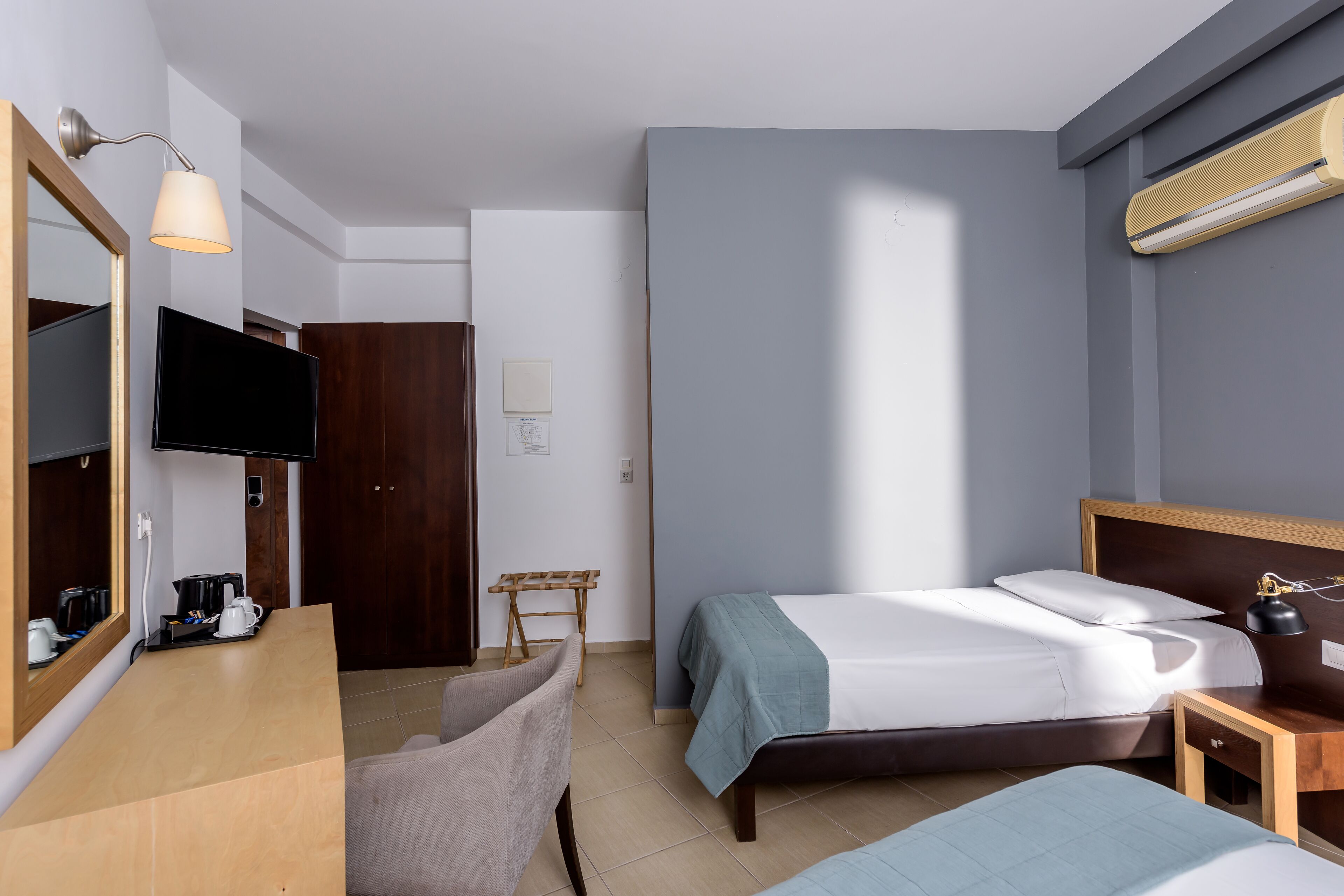 A hotel room with a bed, a desk with a chair, a television, and a mirror.