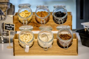 Una barra de desayuno con diversos alimentos en frascos de vidrio, como cereales y frutos secos.