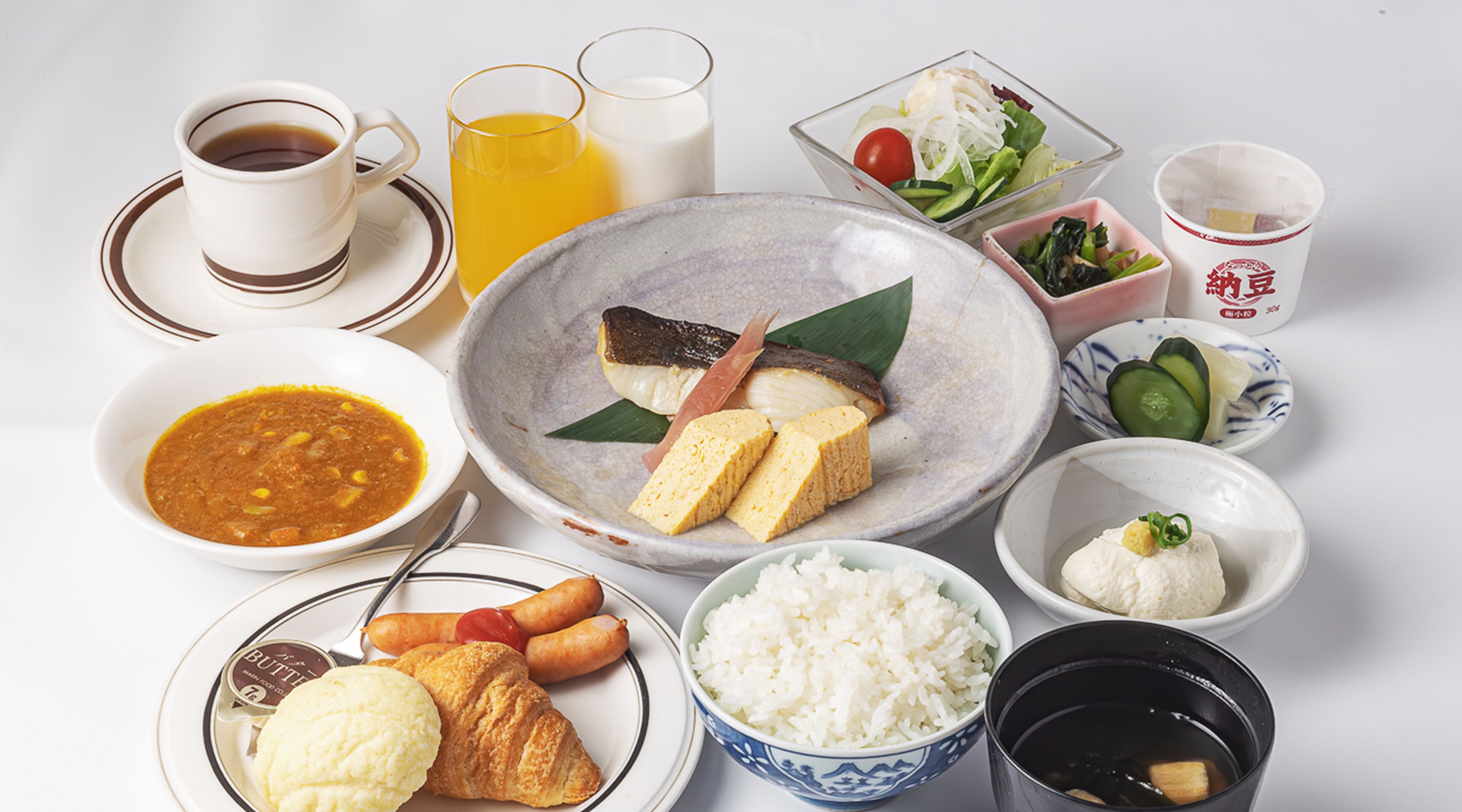 Una mesa con varios platos, incluyendo sopa, arroz, verduras y un croissant.