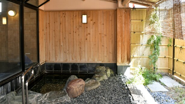 A traditional Japanese onsen with a wooden interior, stone seating, and a bamboo fence. - New Commander Hotel Osaka Neyagawa (Neyagawa)