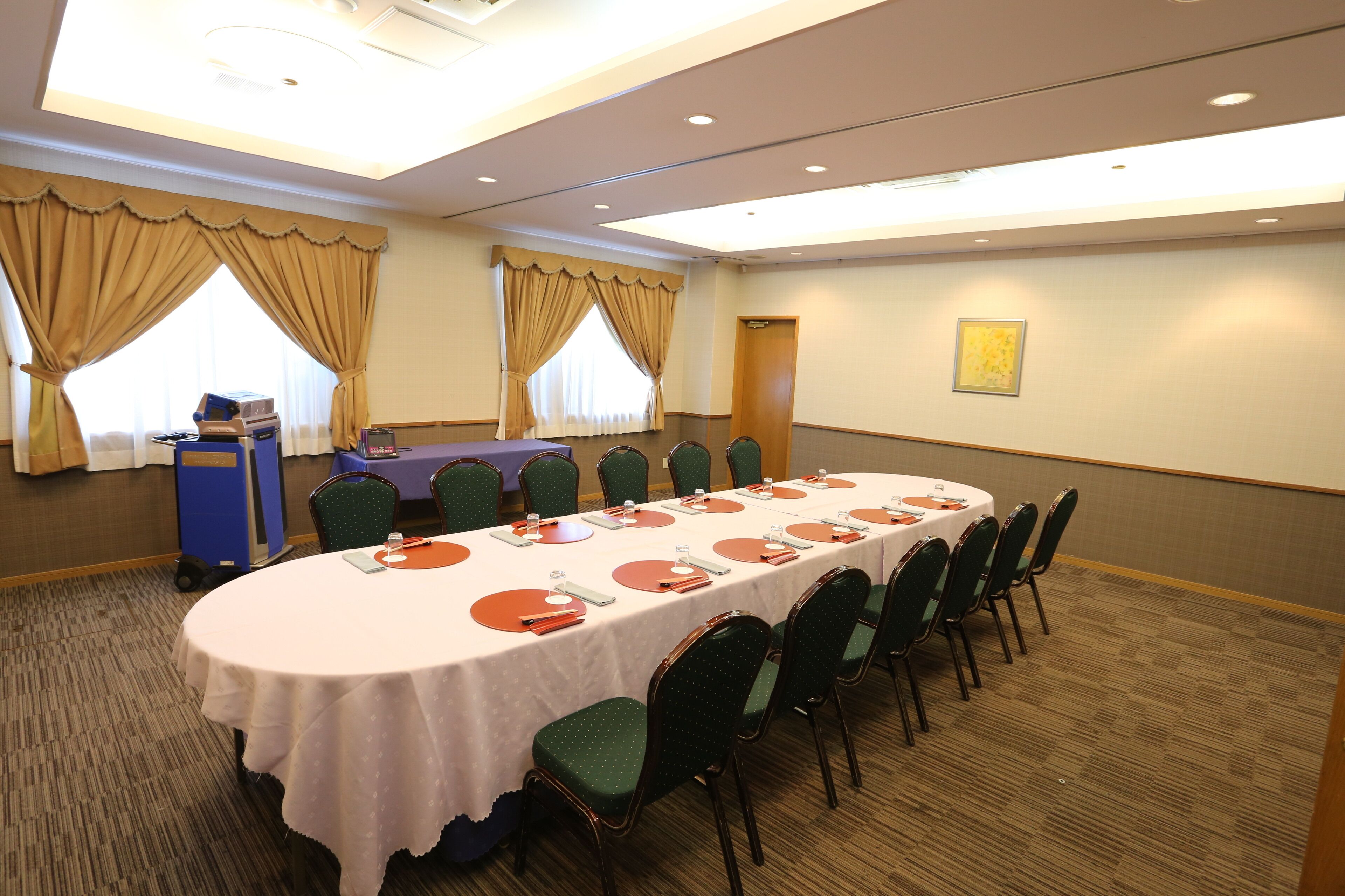 A conference room with a long table, green chairs, and a podium.