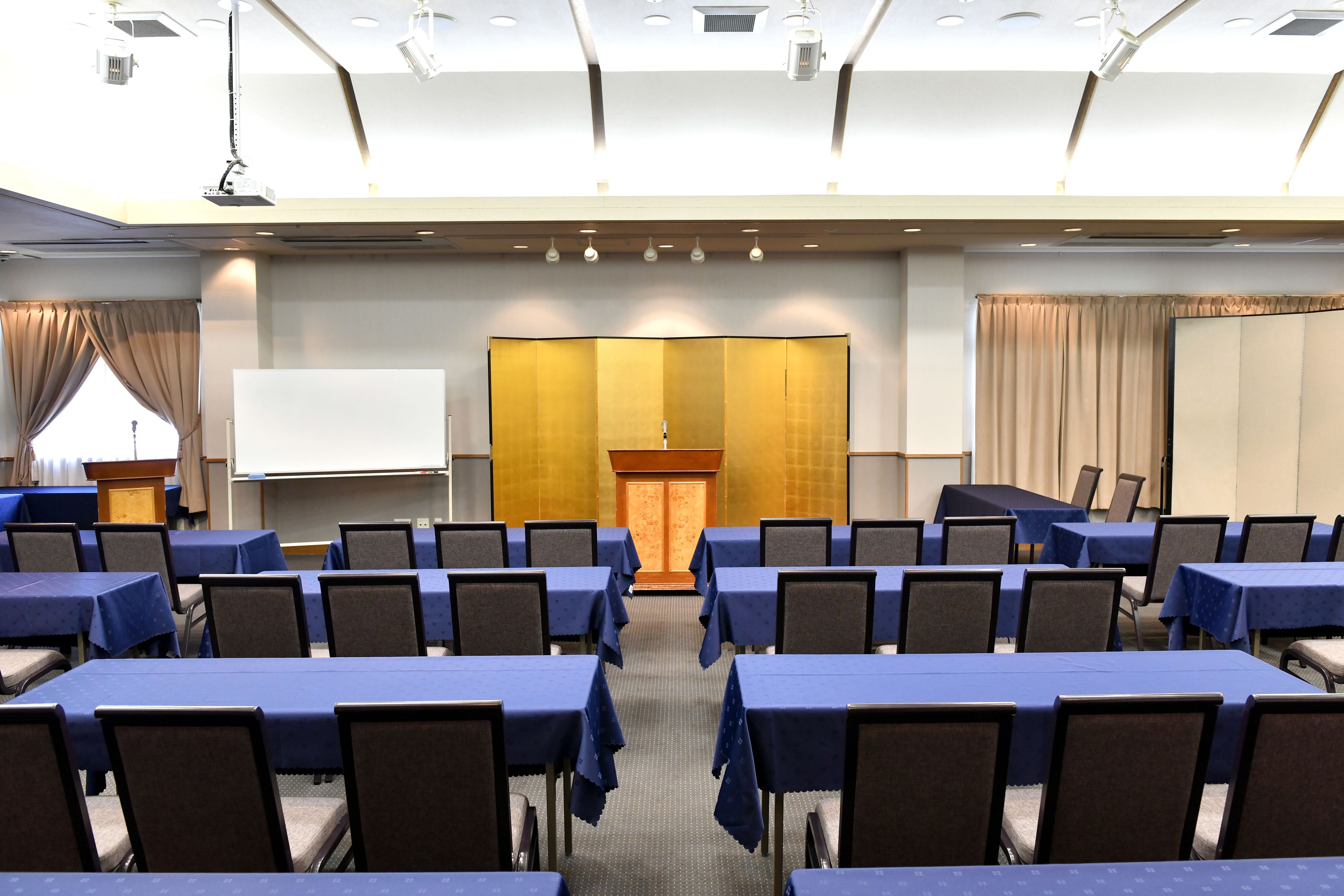 A conference room with rows of tables and chairs, a podium, and a projection screen.