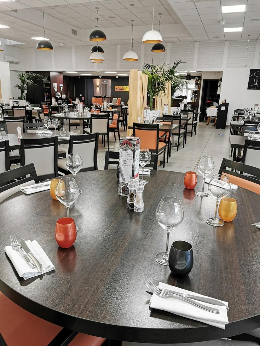 Een restaurant met ronde tafels, stoelen en hangende lampen.