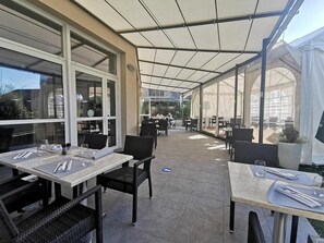 An outdoor patio with tables and chairs, large windows, and a covered area. - Hotel de la Poste (La Cavalerie)