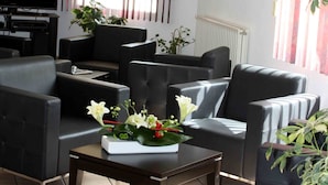 A modern living room with a flat-screen TV, black leather sofas, a coffee table with flowers, and a large window with vertical blinds.