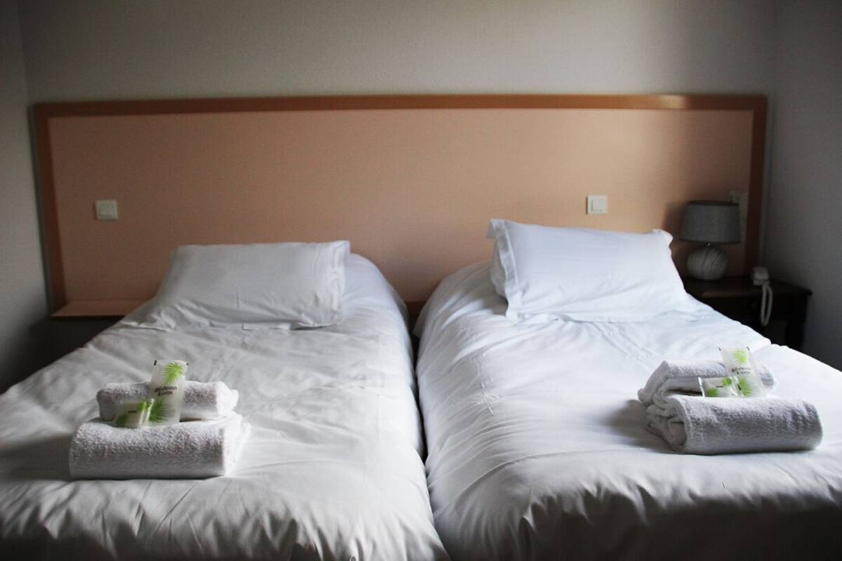 Two single beds with white linens and towels, a wooden headboard, and a nightstand with a lamp.