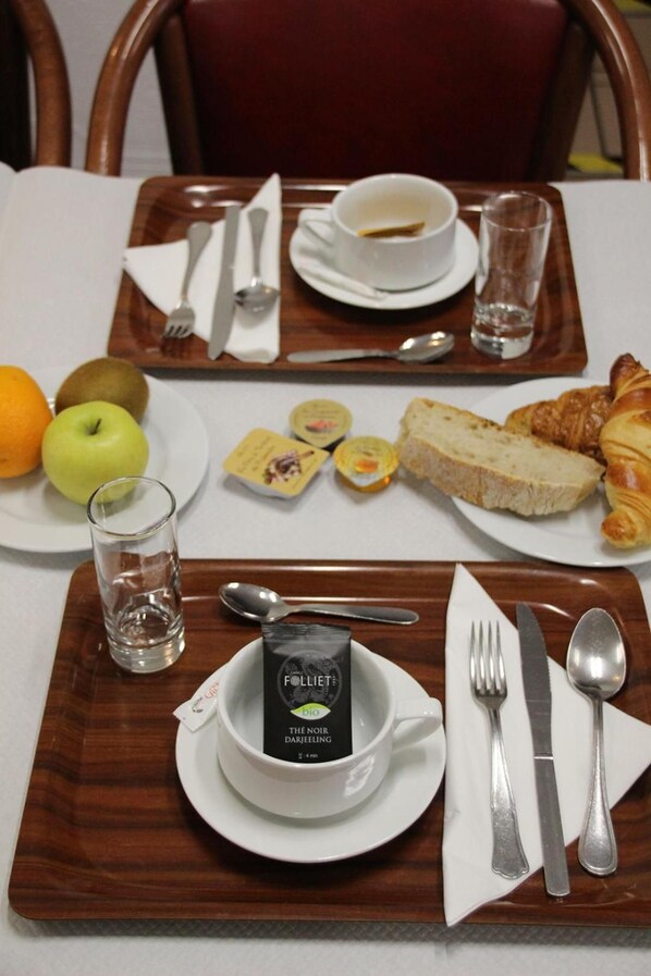 A breakfast tray with a cup of coffee, a glass of water, croissants, bread, an apple, and a kiwi. - Hotel de la Poste (La Cavalerie)