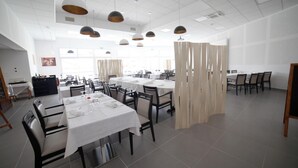 A spacious dining area with multiple tables and chairs, a white ceiling, and pendant lighting.