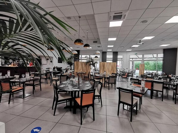 A spacious dining area with multiple tables and chairs, large windows, and a ceiling with recessed lighting. - Hotel de la Poste (La Cavalerie)