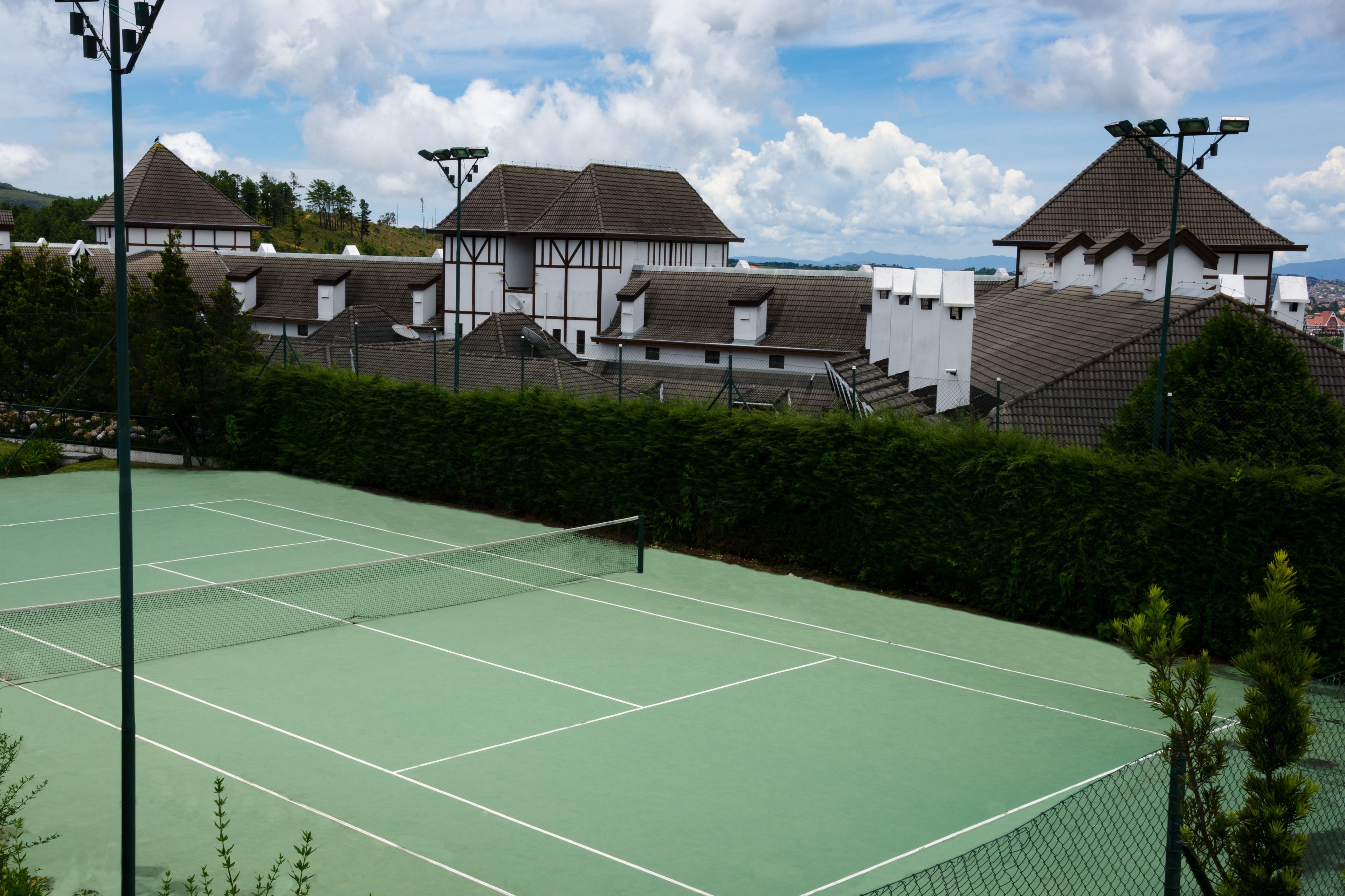 A tennis court with a net, surrounded by a fence and trees.