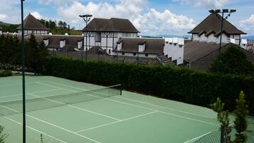 A tennis court with a net, surrounded by a fence and trees.
