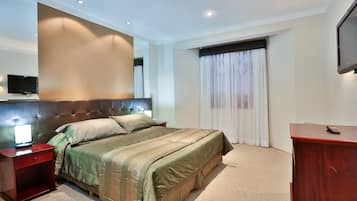 A hotel room with a large bed, a wooden nightstand, a desk, a television, and a window with curtains.