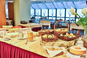 A buffet setup with various food items and baskets, tables with white tablecloths, and a large window with curtains in the background. - Home Green Home (Campos do Jordão)