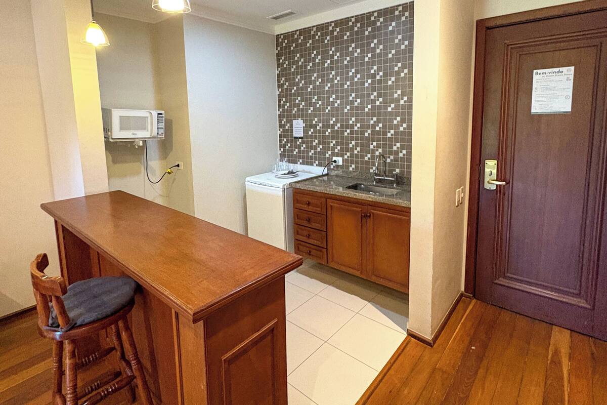 A compact kitchen with a wooden counter, a microwave, a sink, and a patterned backsplash.