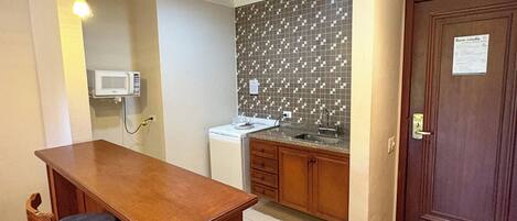A compact kitchen with a wooden counter, a microwave, a sink, and a patterned backsplash.