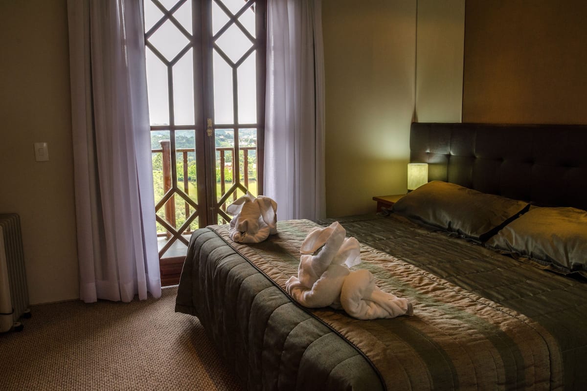 A hotel room with a bed, a window with curtains, a nightstand, and a view of the outdoors.