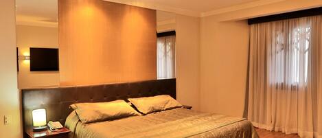 Una habitación de hotel con una cama grande, una mesita de noche con lámpara, un espejo y suelo de madera.
