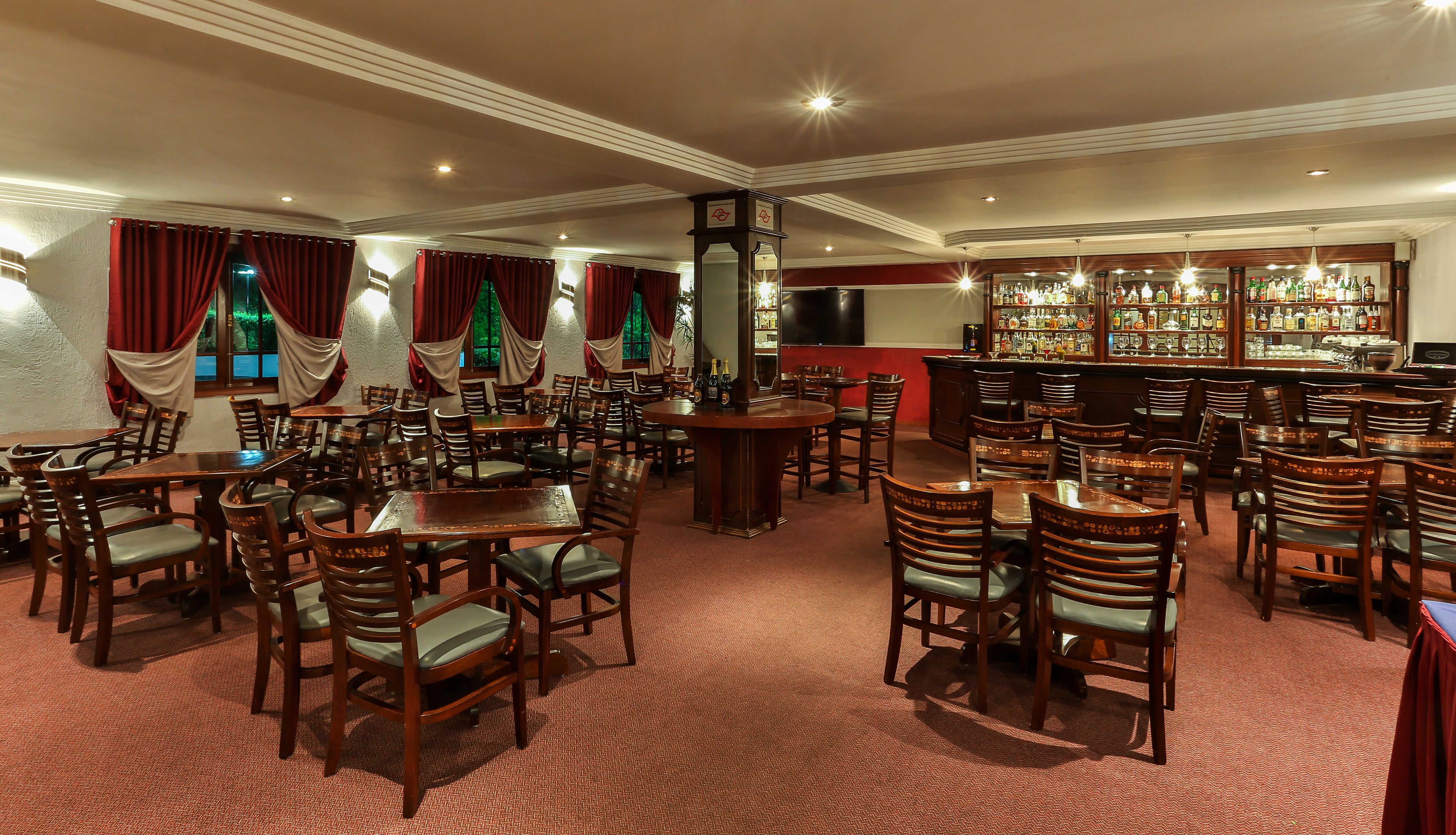 A restaurant with multiple tables and chairs, a bar area with a variety of bottles, and a large screen on the wall.