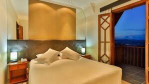 A hotel room with a large bed, bedside lamps, a nightstand, and a view of the city at dusk. - Home Green Home (Campos do Jordão)