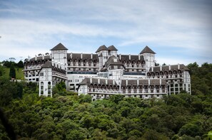 A large, multi-story building with a complex roofline and multiple towers, surrounded by dense greenery. - Home Green Home (Campos do Jordão)